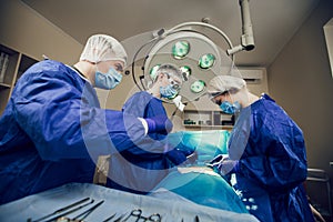 A team of surgeons in a blue uniform operates on a patient in a hospital. Side view of young doctors at work.