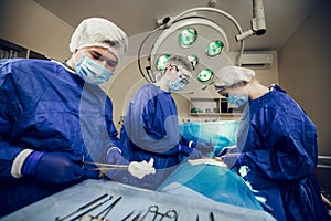 A team of surgeons in a blue uniform operates on a patient in a hospital. Side view of young doctors at work.