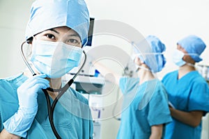 Team of surgeons in the operating room, female surgeon holding stethoscope and looking at camera