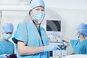 Team of surgeons in the operating room, female surgeon holding stethoscope and looking at camera
