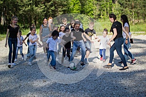 Team of teenagers playing yard football with a children team at sunny day