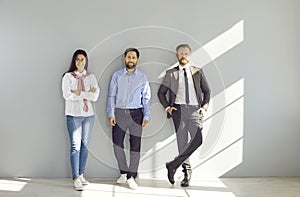 Team of three business people standing together by a gray wall at work in the office