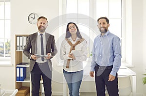 Team of three cheerful young business people standing in their office and smiling