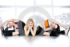 Team of three females posing, sitting in splits in fitness class