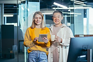 Team of two Asian male and female workers take a break, look at the camera and smile, use a tablet to discuss a joint business