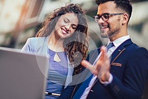 Two business people working together outdoors using laptop