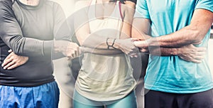 A team of two men and a woman in the middle in sportswear hold hands as a symbol of team spirit and unity