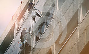 Team of workers painting wall high rise building. Painters are painting exterior office building with roller. Dangerous jobs