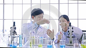 Team of young Asian female and male colleague scientists using microscope and holding a test tube in life science