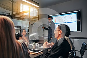 Team of young smiling business people in conference room discussing project. A speaker stands next to the flipchart and shows the