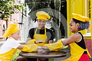 Teambuilding of multinational children cooks in chefs hat and yellow apron uniform put hands on each other, having fun