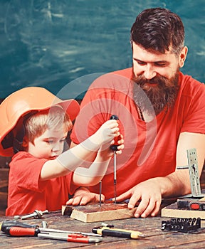 Teamwork and assistance concept. Father, parent with beard teaching little son to use tool screwdriver. Boy, child busy