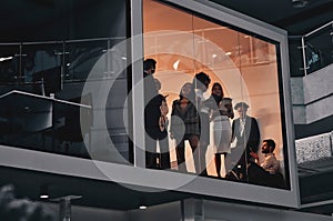 Teamwork. Behind the glass in the meeting room in a spacious large business center, a team of young people stand and discuss the