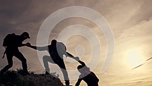 Teamwork of the business group. Male partners climb to the top. Silhouette of a helping hand at sunset. The concept of