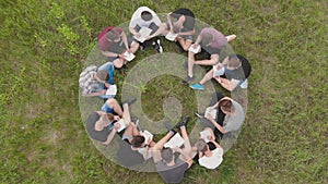 Teamwork concept. A group of high school students sit on the grass in a circle. Drone view.