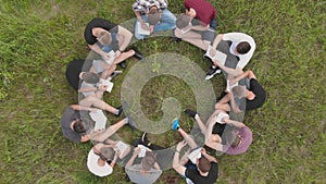 Teamwork concept. A group of high school students sit on the grass in a circle. Drone view.