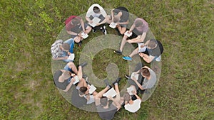 Teamwork concept. A group of high school students sit on the grass in a circle. Drone view.