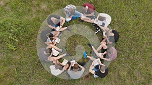 Teamwork concept. A group of high school students sit on the grass in a circle. Drone view.