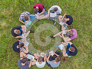 Teamwork concept. A group of high school students sit on the grass in a circle and scatter in different directions