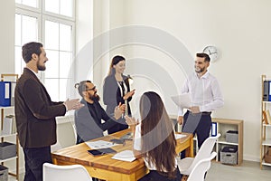 Group of smiling business people applauding to coworker after presentation of new project in office