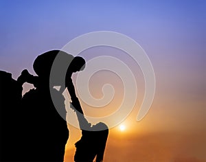 Teamwork couple helping hand trust assistance silhouette in mountains, sunset.