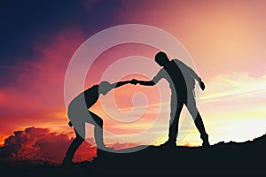 Teamwork couple helping hiking each other silhouette on mountain