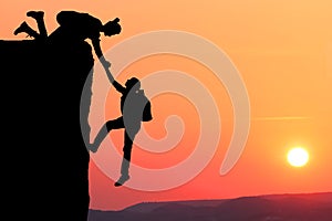 Teamwork couple hiking help each other trust assistance silhouette in mountains, sunset. Teamwork of man and woman hiker helping e