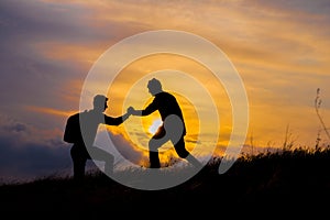 Teamwork couple hiking help each other trust assistance silhouette in mountains, sunset. Teamwork of two men hiker helping each