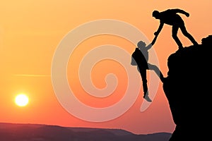 Teamwork couple hiking help each other trust assistance silhouette in mountains, sunset. Teamwork of two men hiker helping each ot