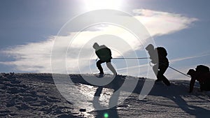 Teamwork desire to win. Climbers on a rope help a friend climb to the top of the hill. Silhouette of travelers in winter