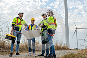 Teamwork engineer worker wearing safety uniform holding and reading blueprint at wind turbine field renewable energy. technology