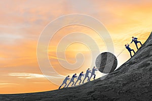 Teamwork example with business people pushing stone to top photo