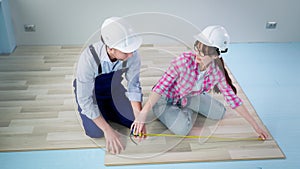 teamwork female and male wearing protective helmets doing construction work and laying laminate flooring during