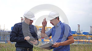 Teamwork. Industry gas production station concept. Slow motion video. Two engineers in helmets are studying working with