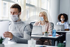 Teamwork on project. Multiracial employees in protective masks work on laptops at desks with antiseptics, focus on lady