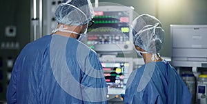 Teamwork, screen monitor or surgeon in surgery procedure or healthcare operation in hospital. Night, back view or