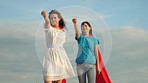 Teamwork superheroes. two girls in red cloaks of superheroes stand against a blue sky, the wind inflates a cloak. Mom