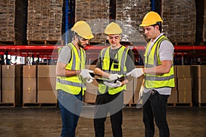 Teamwork of Three warehouse workers in uniform wearing yellow safety helmets standing working talking and discussing in a large