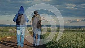 Teamwork travel. two man hikers with backpacks walk along a trail next to a field with green grass in nature. concept