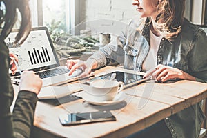 Teamwork. Two young business woman sitting at table in coffee shop, look at chart on laptop screen and develop business plan.