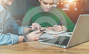 Teamwork. Two young business women sitting at desk in office and working. On table is laptop and paper charts.