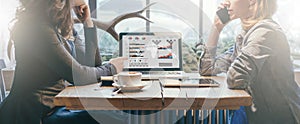 Teamwork, two young businesswomen sitting across table from each other. On table laptop, coffee cup and tablet computer.