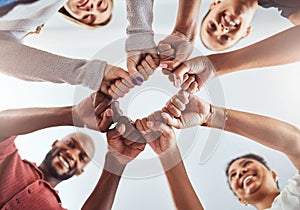 Teamwork, unity and hands or fist for support, trust and community below blue sky. Diversity group men and women friends