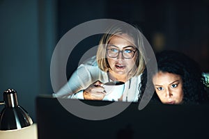 Teamwork will take them through the night. two colleagues using a computer together during a late night at work.