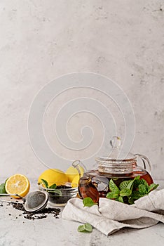 Teapot with black tea decorated with mint leaves, lemons and dry tea leaves front view with copy space