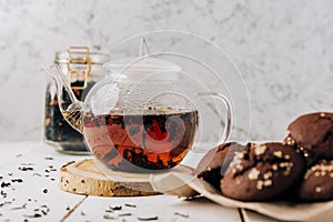 Teapot with black tea and homemade chocolate cookies on a white natural wooden background