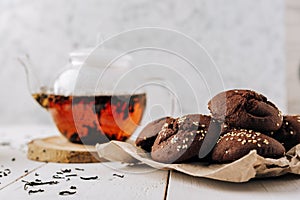 Teapot with black tea and homemade chocolate cookies on a white natural wooden background