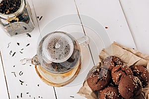 Teapot with black tea and homemade chocolate cookies on a white natural wooden background