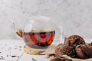 Teapot with black tea and homemade chocolate cookies on a white natural wooden background