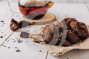 Teapot with black tea and homemade chocolate cookies on a white natural wooden background